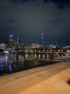 the city skyline is lit up at night with boats in the water and lights on