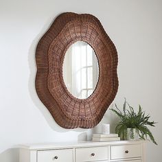 a round mirror hanging on the wall above a dresser with drawers and a potted plant