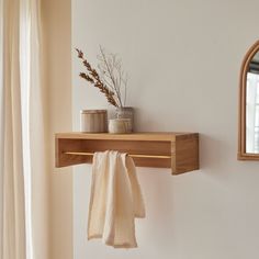 a towel hanging on a wooden shelf next to a mirror and potted plant in a vase