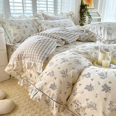 a bed with white and blue comforters in front of a window filled with pillows