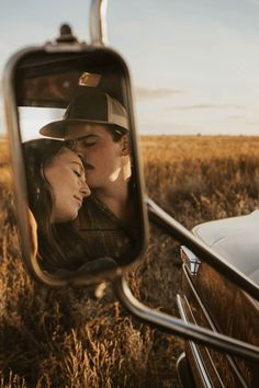 a man and woman kissing in front of a car mirror on the side of a road