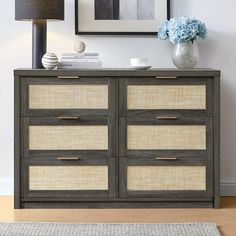 a gray and beige dresser with baskets on the bottom, blue hydrangeas in vase next to it