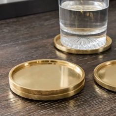 two gold coasters sitting on top of a wooden table next to a glass filled with water