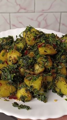 a white plate topped with potatoes covered in greens and seasoning next to a brick wall