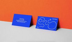 two blue business cards sitting on top of each other in front of an orange wall