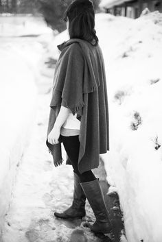 a woman standing in the snow wearing boots and a ponchy over her shoulder