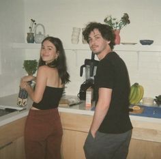 a man and woman standing next to each other in a kitchen near a counter top