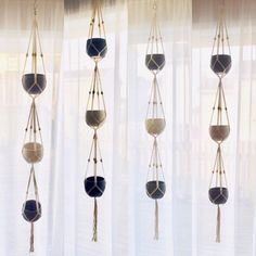 four hanging planters in front of a window with sheer curtains behind them, each containing different shades of blue and white