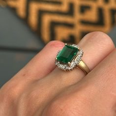 a close up of a person's hand wearing a ring with an emerald and diamond