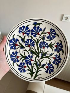 a hand holding a blue and white plate with red, green, and blue flowers on it