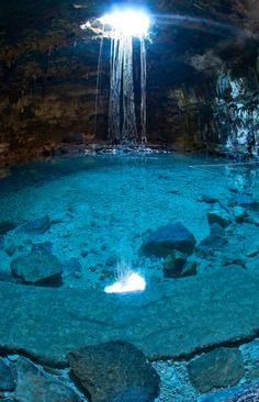 the inside of a cave with blue water and rocks on the ground, under a bright light