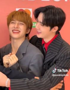 two young men standing next to each other in front of a red wall with the words i love you written on it