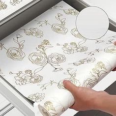 a hand is holding a roll of wrapping paper in front of a drawer with flowers on it