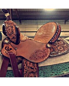 a horse saddle with an intricate design on it's back and seat, sitting in a stable