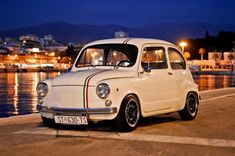 an old white car is parked on the side of the road by the water at night