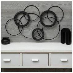 a white dresser topped with drawers next to a metal wall art piece on top of a wooden