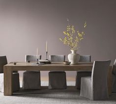 a dining table with chairs and a vase on the top, in front of a purple wall