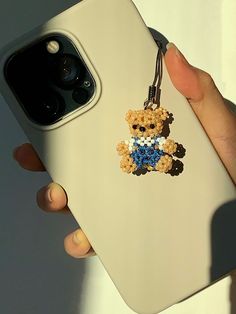 a person holding a cell phone with a teddy bear keychain on it