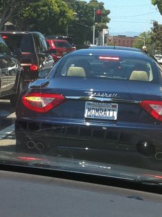 the back end of a blue car driving down a street next to traffic lights and trees