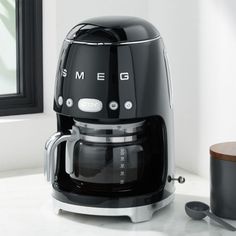 a black and silver coffee maker sitting on top of a counter next to a cup