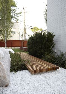 a wooden bench sitting in the middle of a garden next to a rock and shrubbery