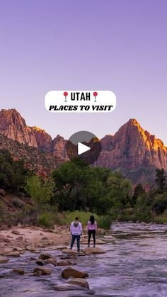 two people standing on rocks in the middle of a river with mountains in the background