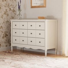 a white dresser sitting next to a window in a room with floral wallpaper on the walls