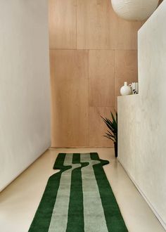 a green rug on the floor in front of a wooden wall and white vases