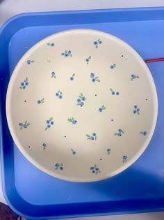 a white bowl with blue flowers on it sitting on a blue tray next to a red spoon