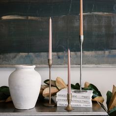 a white vase sitting on top of a table next to two candles and some books