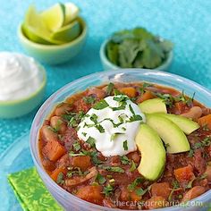 a bowl of chili with avocado, sour cream and cilantro on the side