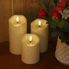 three white candles sitting on top of a table next to a vase filled with flowers