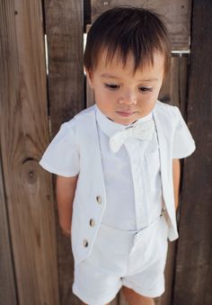 a little boy wearing a white shirt and bow tie standing in front of a wooden fence