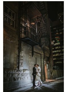 a bride and groom standing in front of an old building at night with their arms around each other