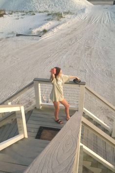 a woman standing on the side of a snow covered ski slope while talking on a cell phone