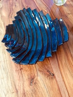 a stack of blue glass plates sitting on top of a wooden table next to a vase