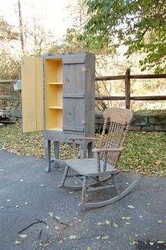 a wooden rocking chair next to a cabinet on the ground in front of a fence