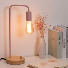 a light that is on top of a desk next to books and a vase with flowers