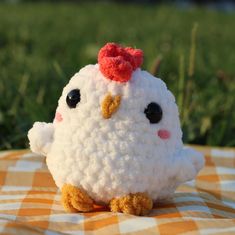 a small white stuffed chicken sitting on top of a checkered tablecloth covered ground