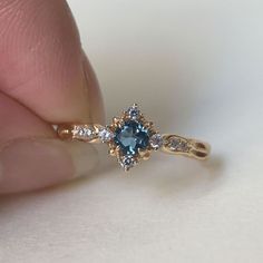 a person is holding a ring with a blue stone in the middle and two white diamonds around it