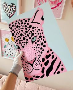 a person holding up a paper cut out of a pink and black leopard head on a wall