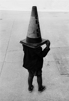 a little boy wearing a cone hat on his head while walking down the street in black and white