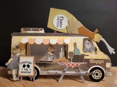 a paper model of a food truck on a wooden table next to a black wall