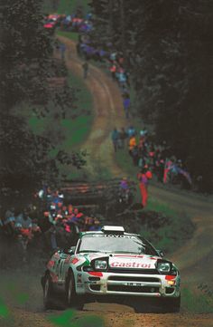 a rally car driving down a dirt road in front of people on the side of a hill