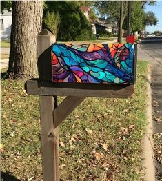 a colorful stained glass mailbox sitting on the side of a wooden bench next to a tree