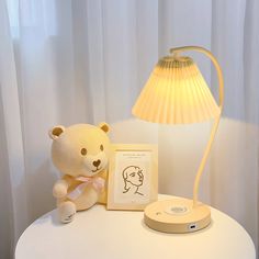 a teddy bear sitting on a table next to a lamp with a picture frame in front of it