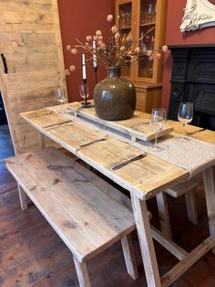 a wooden table with two benches and a vase on it, in front of a fireplace