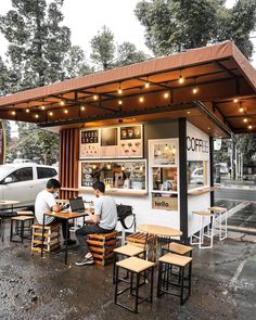 two men sitting at tables in front of a coffee shop with lights on the roof