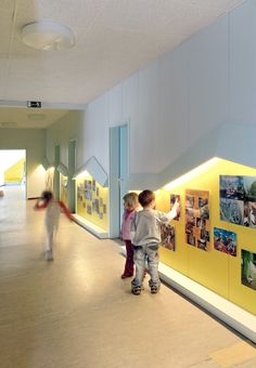 two children are walking down the hallway with pictures on the wall and lights above them