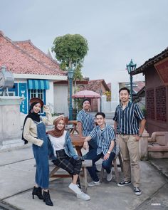 a group of people sitting around a wooden table in front of a building with umbrellas